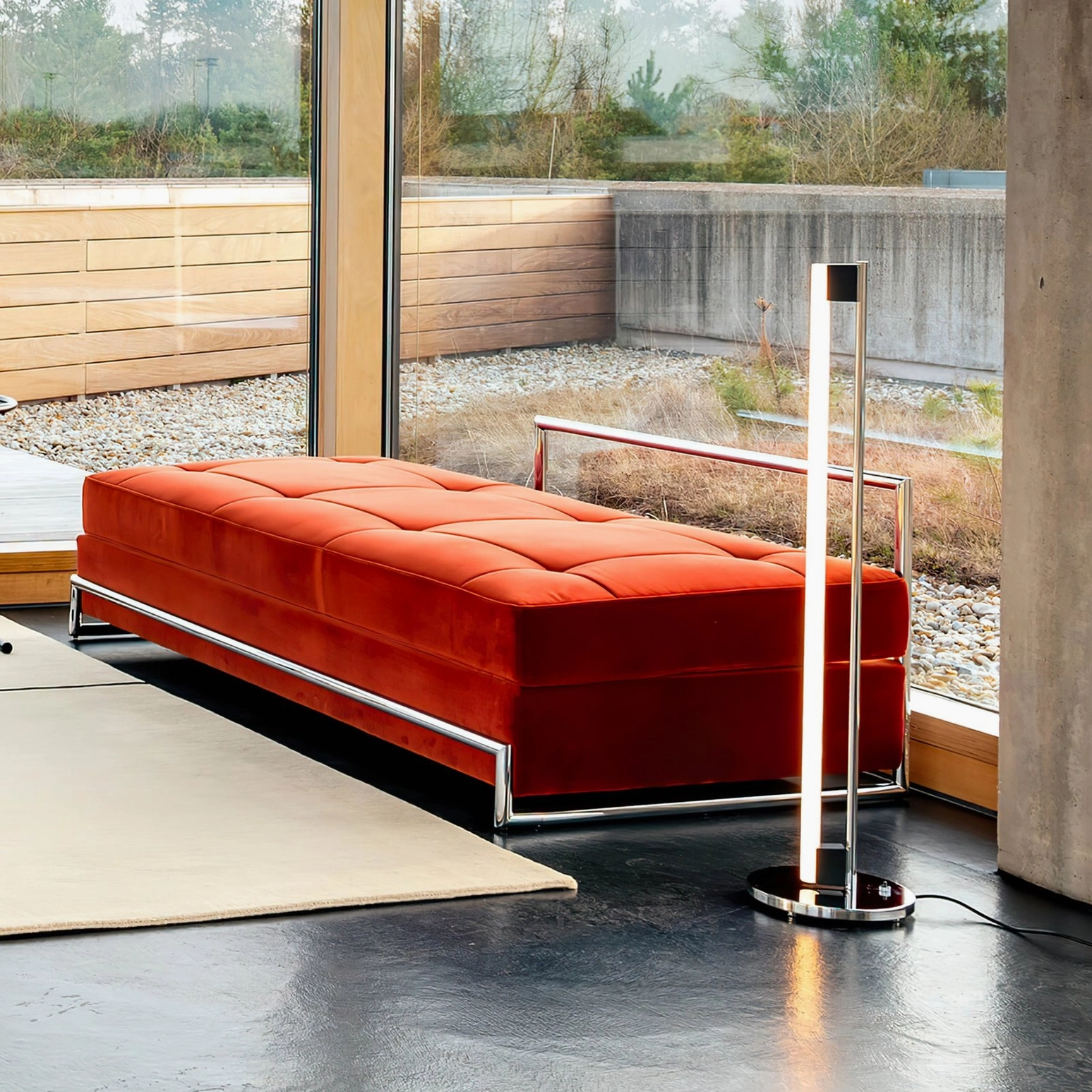 Low-angle view of chrome tube LED lamp in sunlit living room with red tufted daybed showcasing minimalist luxury