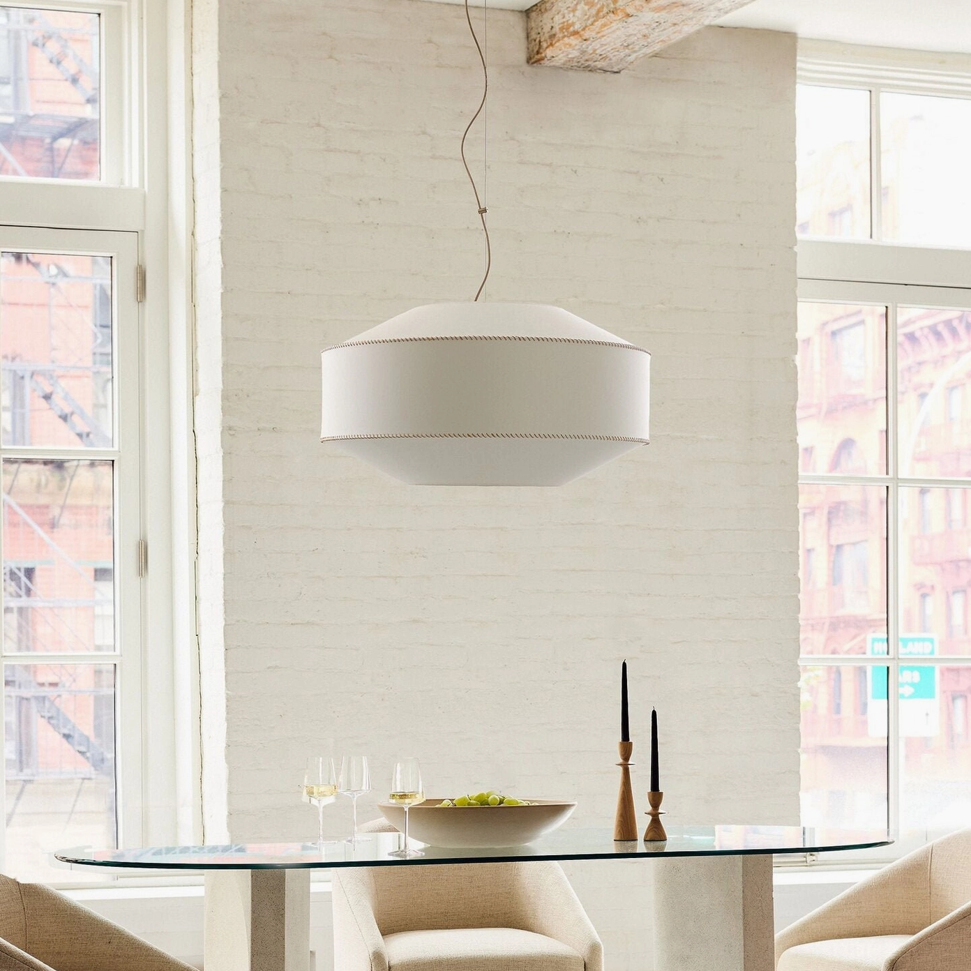 Warm linen pendant light in industrial dining room above glass table creating architectural focal point