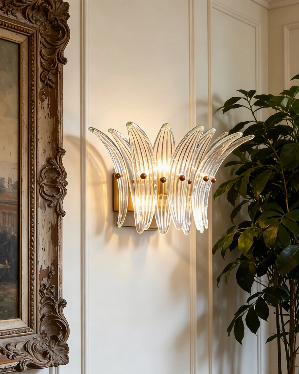 Clear fluted glass Smeralda sconce mounted beside vintage frame on paneled wall with greenery