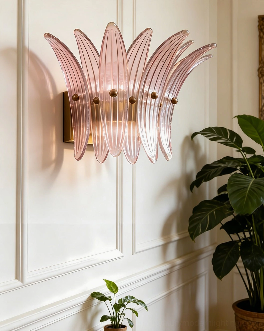 Pink fluted glass Smeralda sconce with warm glow and petal texture on paneled wall with plants