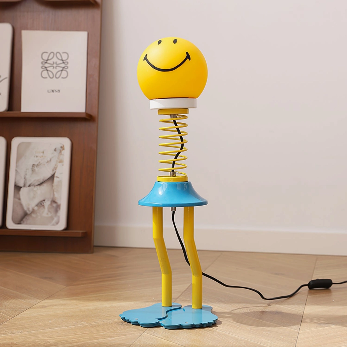 Smiley face spring lamp three-quarter angle on wooden shelf, yellow shade with blue barefoot base, home interior styling