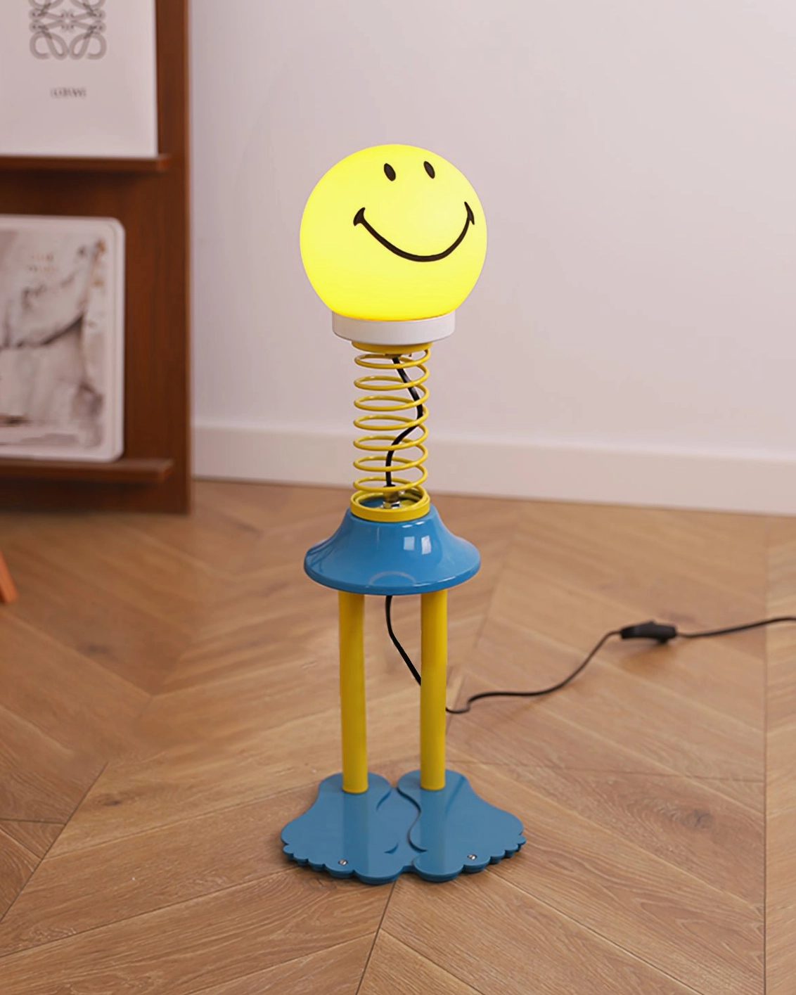 Side view of spiral spring smiley face lamp showing metal coil stem and yellow legs on herringbone wood floor