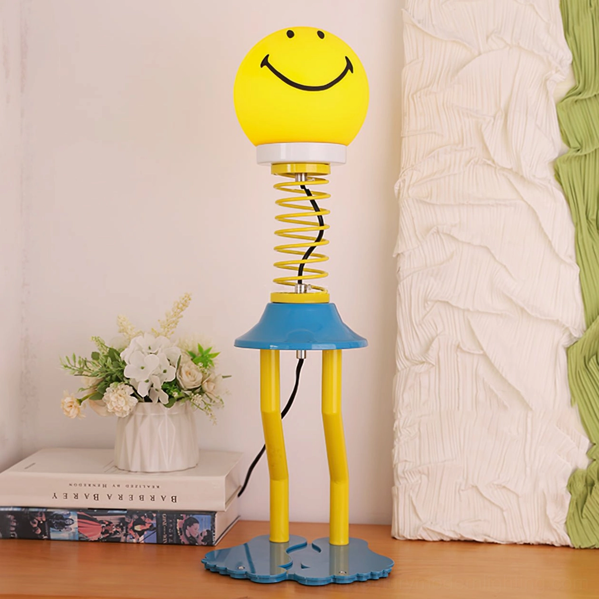 Smiley face table lamp side view with flower vase and stacked books, cozy home tabletop styling