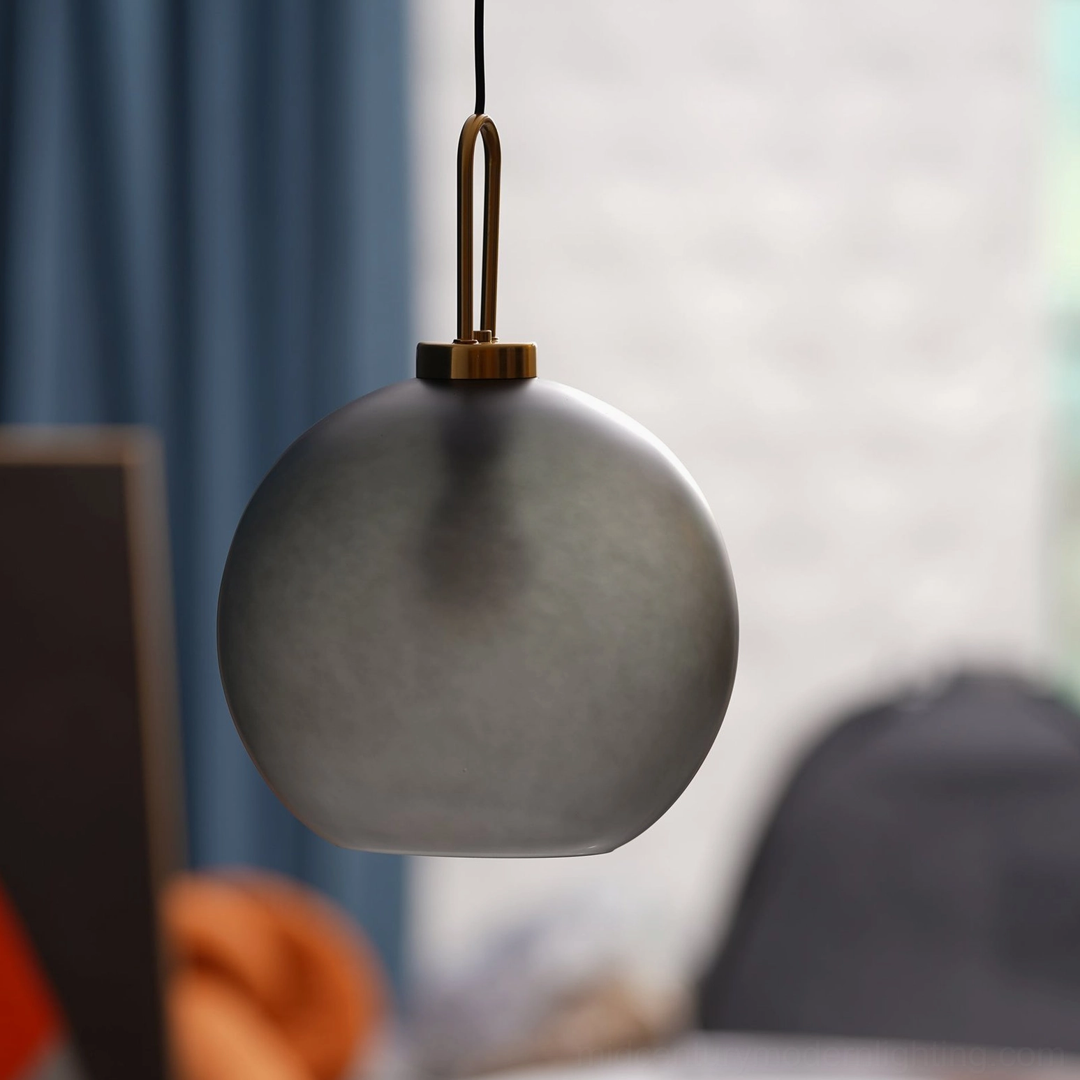 Close-up low-angle view of matte dark gray spherical smoked glass pendant with brass fixture in living space