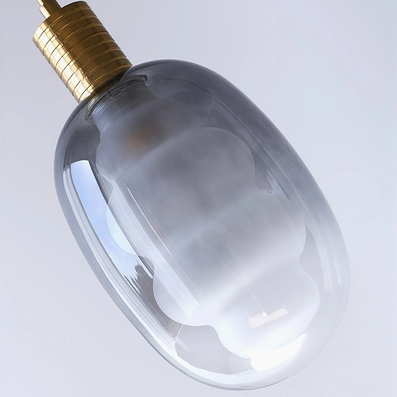 Smoky gray sculptural glass pendant, low-angle close-up, ribbed brass metal top, frosted shade detail