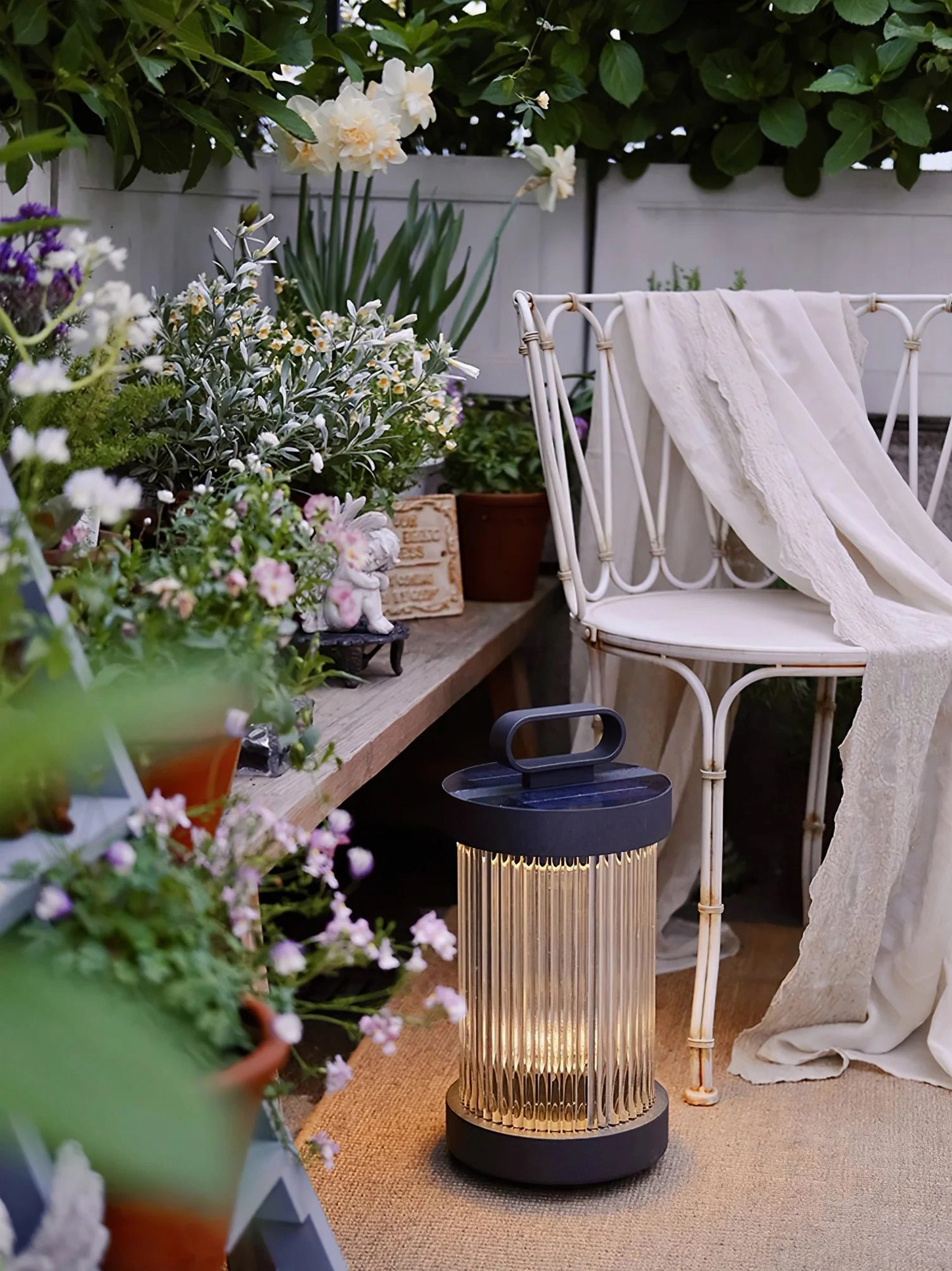 Solar table lantern lamp with black metal base in flower-filled outdoor patio garden