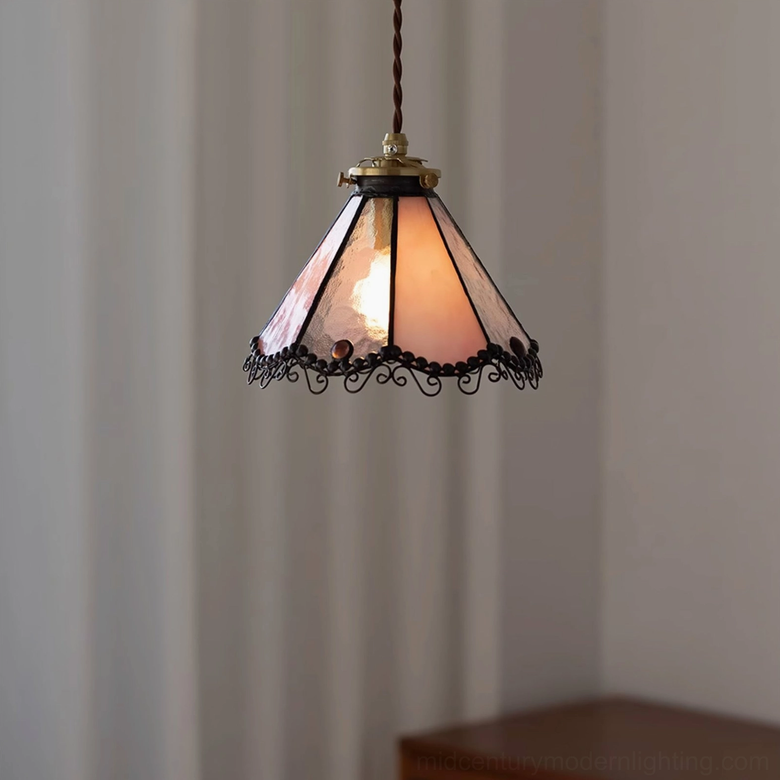 Sonoma Tiffany pendant lamp in peach-pink stained glass hanging in modern home with lit warm bulb and sheer window drapery