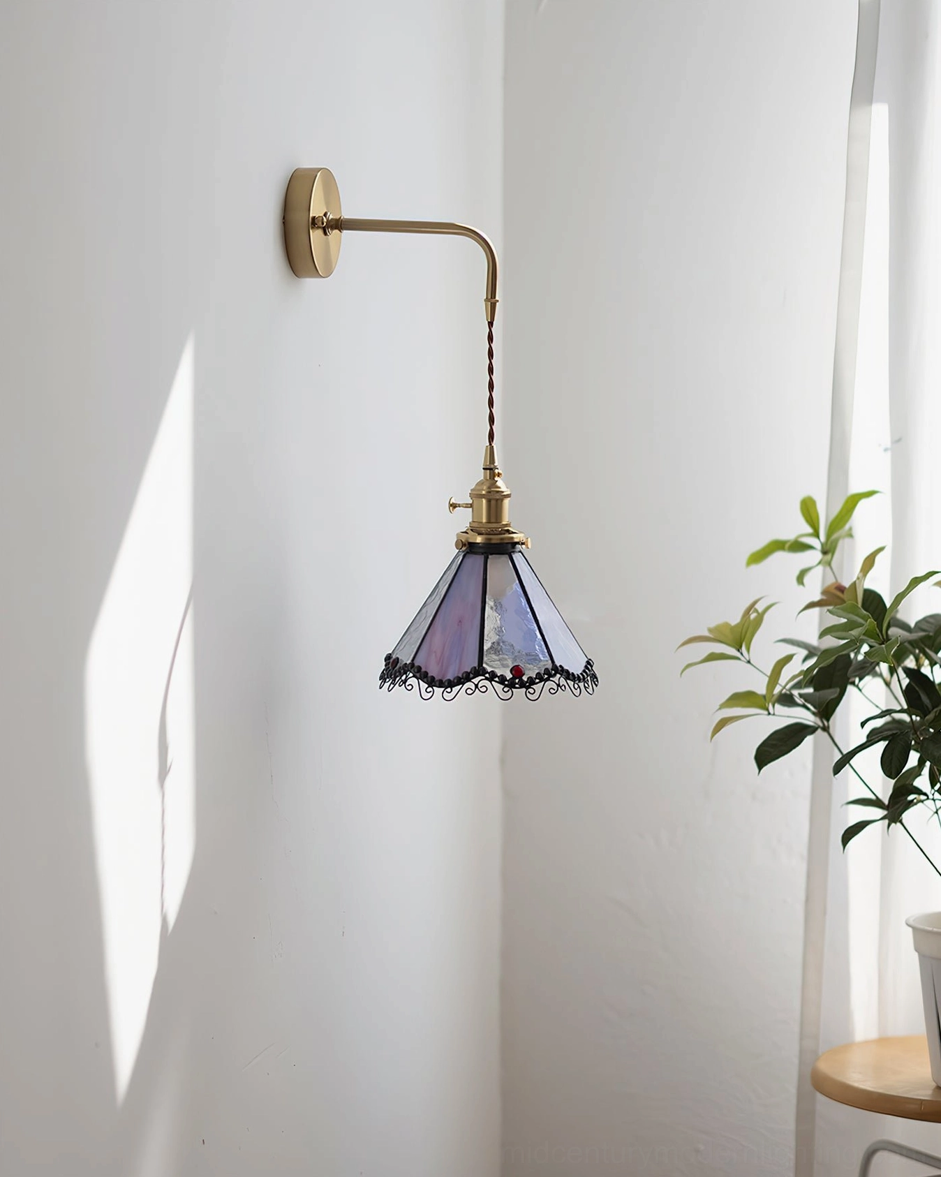 Long-arm Sonoma Tiffany stained glass wall lamp with purple shade and brass mounting bracket in indoor corner setting with green plant