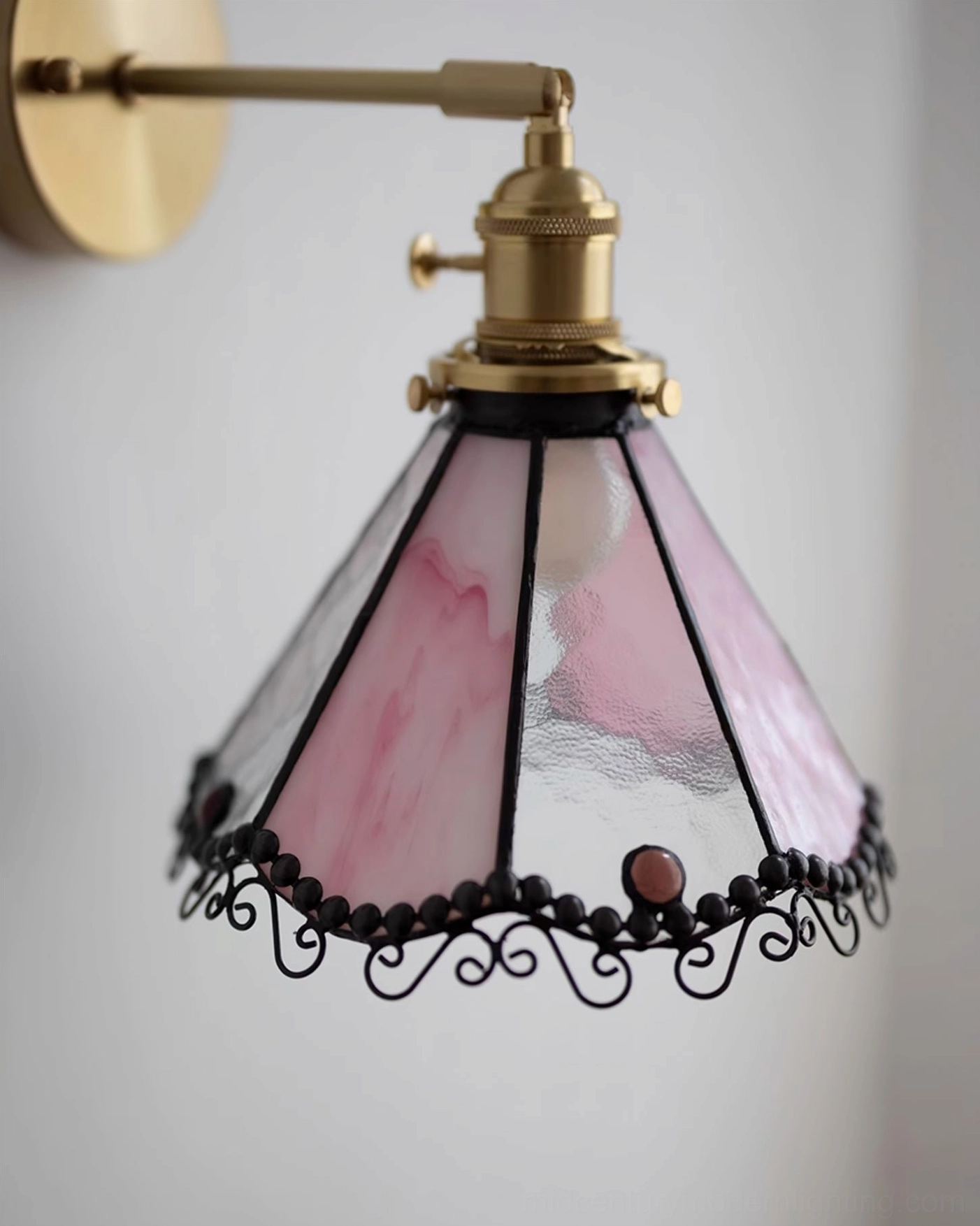 Close-up front view of Sonoma Tiffany wall sconce in pink stained glass with brass hardware and ornamental black edging