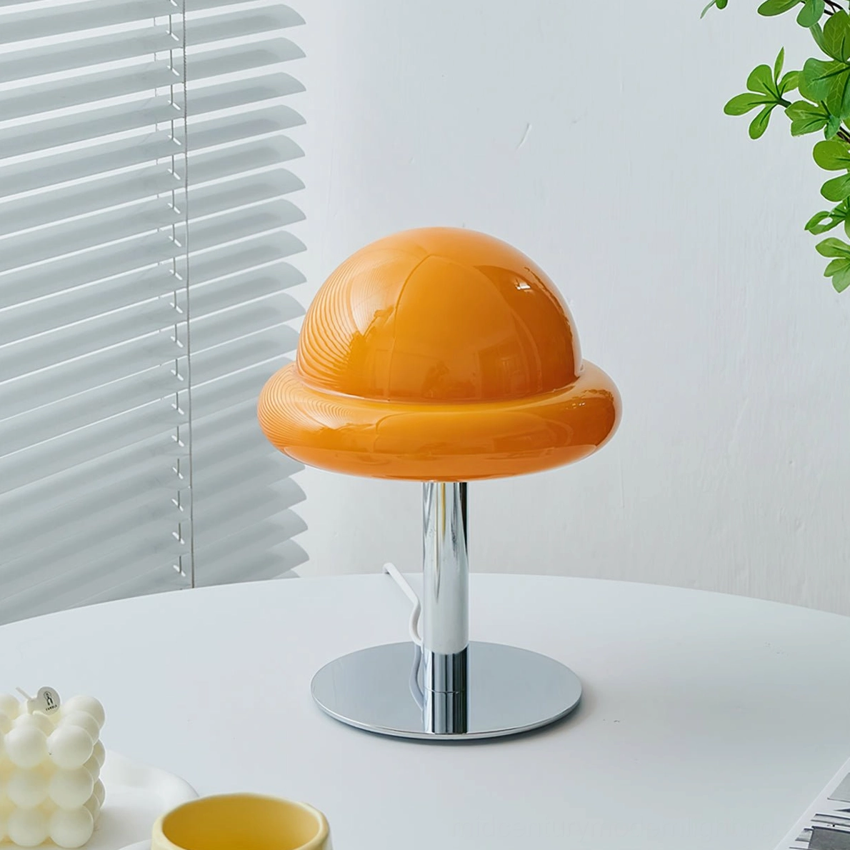 Mid-century modern mushroom lamp with three-quarter frontal view on white round table with candle and blind backdrop