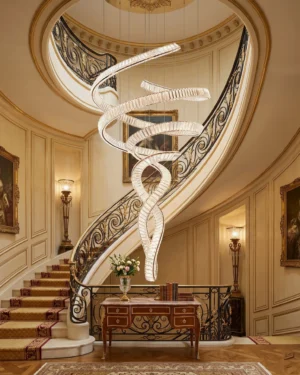 Modern spiral crystal chandelier installed in luxury duplex foyer above dark wooden staircase with metal railings, warm ambient lighting