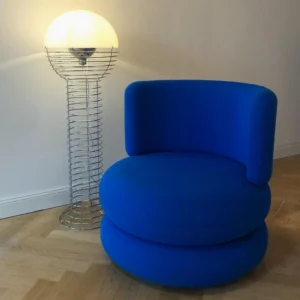 Spiral wire floor lamp in modern living room with blue accent chair, chrome wire frame with warm glowing hemispherical shade