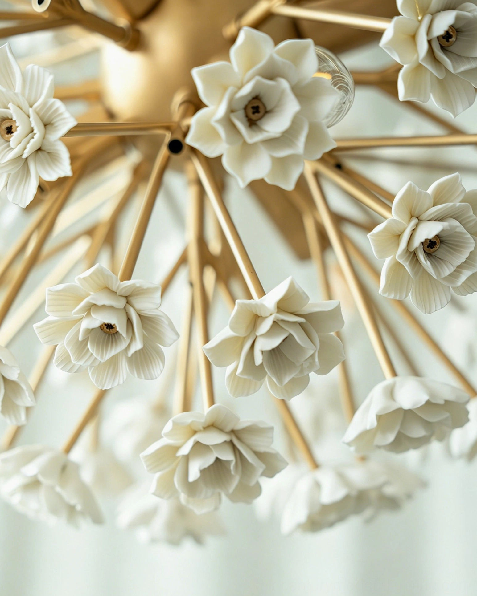 Overhead close-up of delicate white ceramic flowers and polished brass hardware on sputnik chandelier