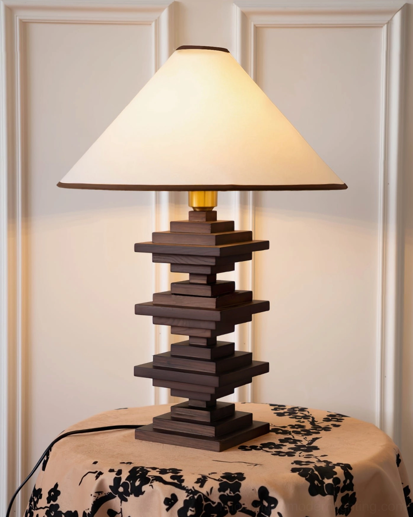 Wooden block tower lamp displayed on side table with black floral tablecloth and indoor wall backdrop