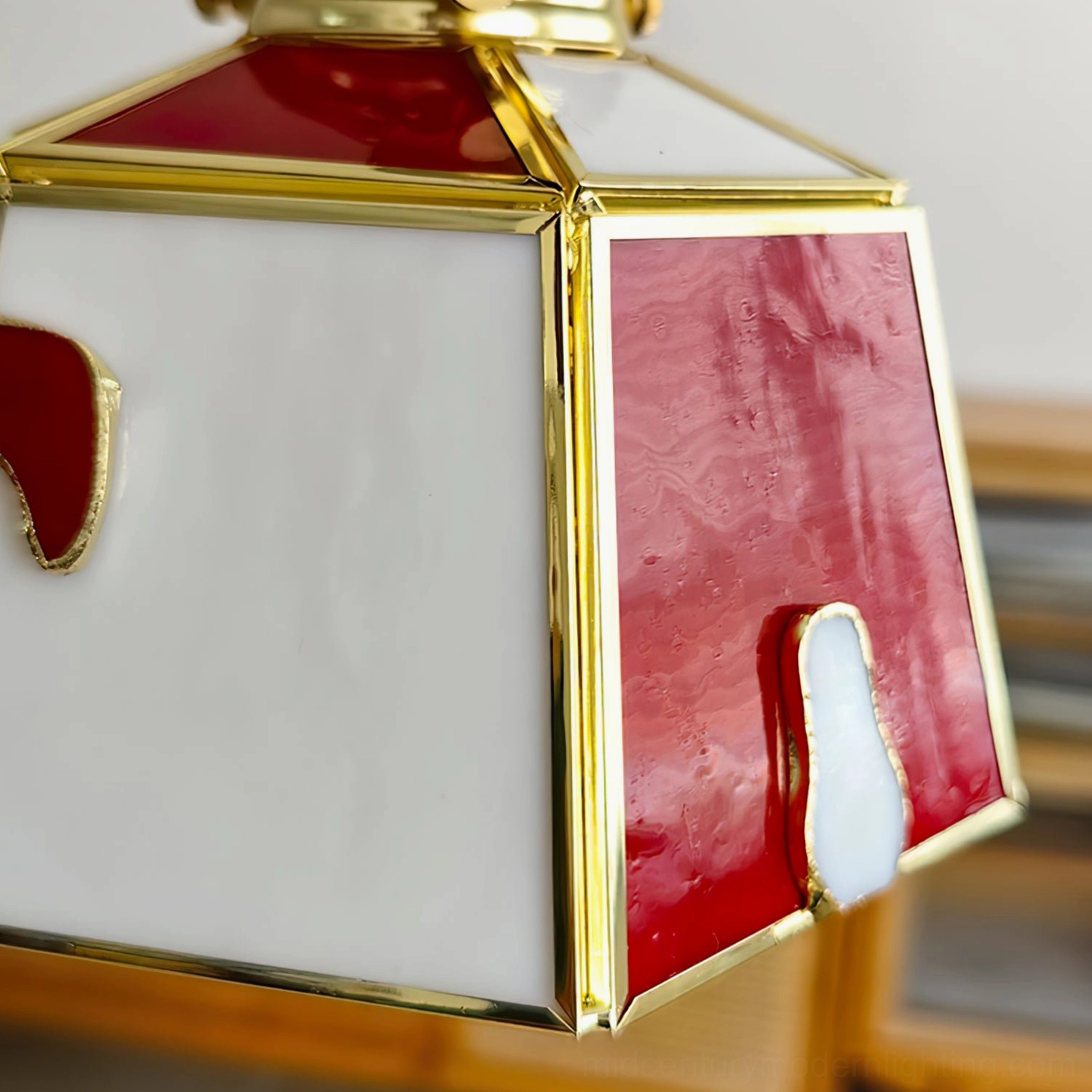 Close-up top view of stained glass pendant shade showing gold brass frame and red-white glass inlays on wooden surface