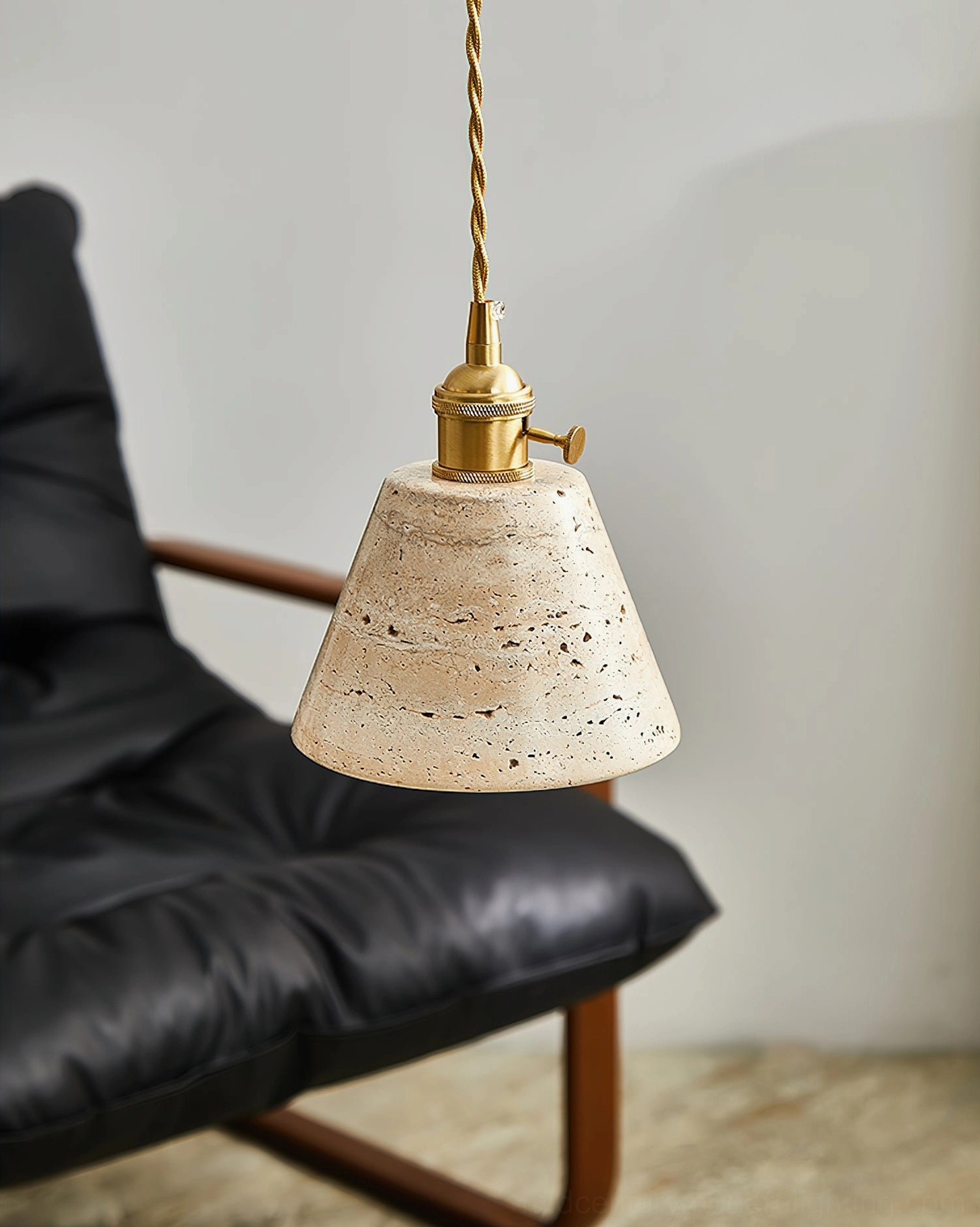 Stella conical travertine pendant light close-up side view with brass turn switch and natural stone surface detail, leather armchair setting