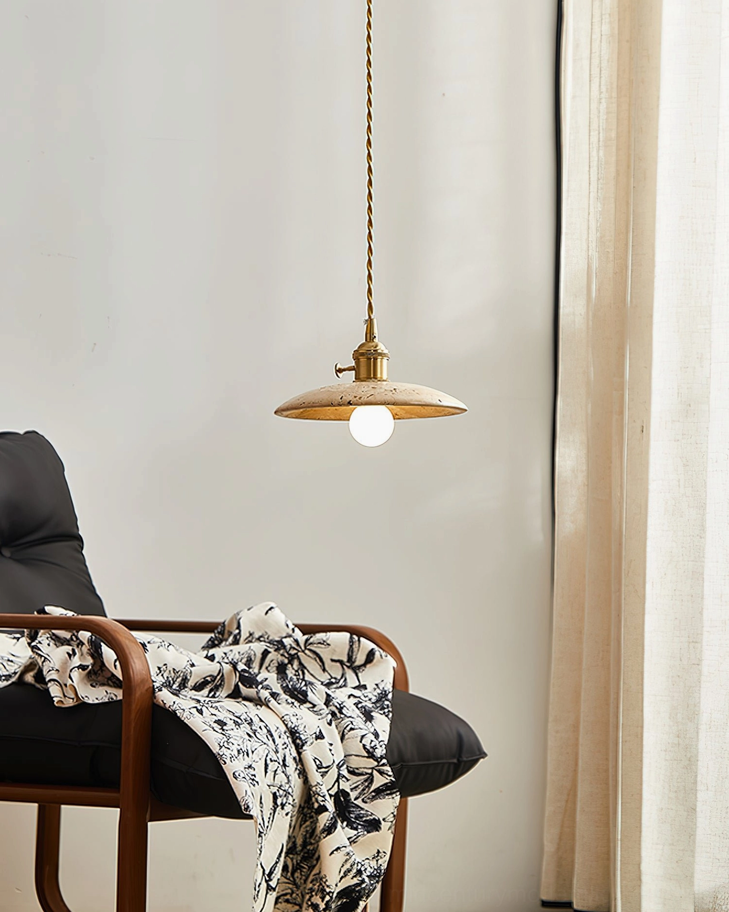 Stella travertine pendant light side view in contemporary living room with lounge chair, flat disc design with brass hardware and exposed bulb