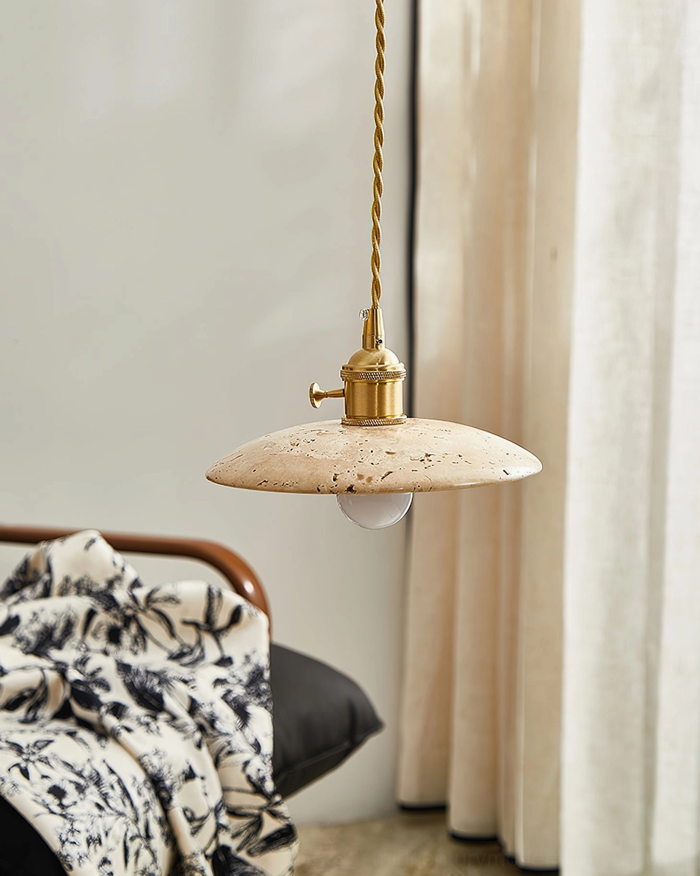 Stella flat disc travertine pendant light with twisted brass cord and globe bulb, low frontal view in living room with neutral throw blanket palette