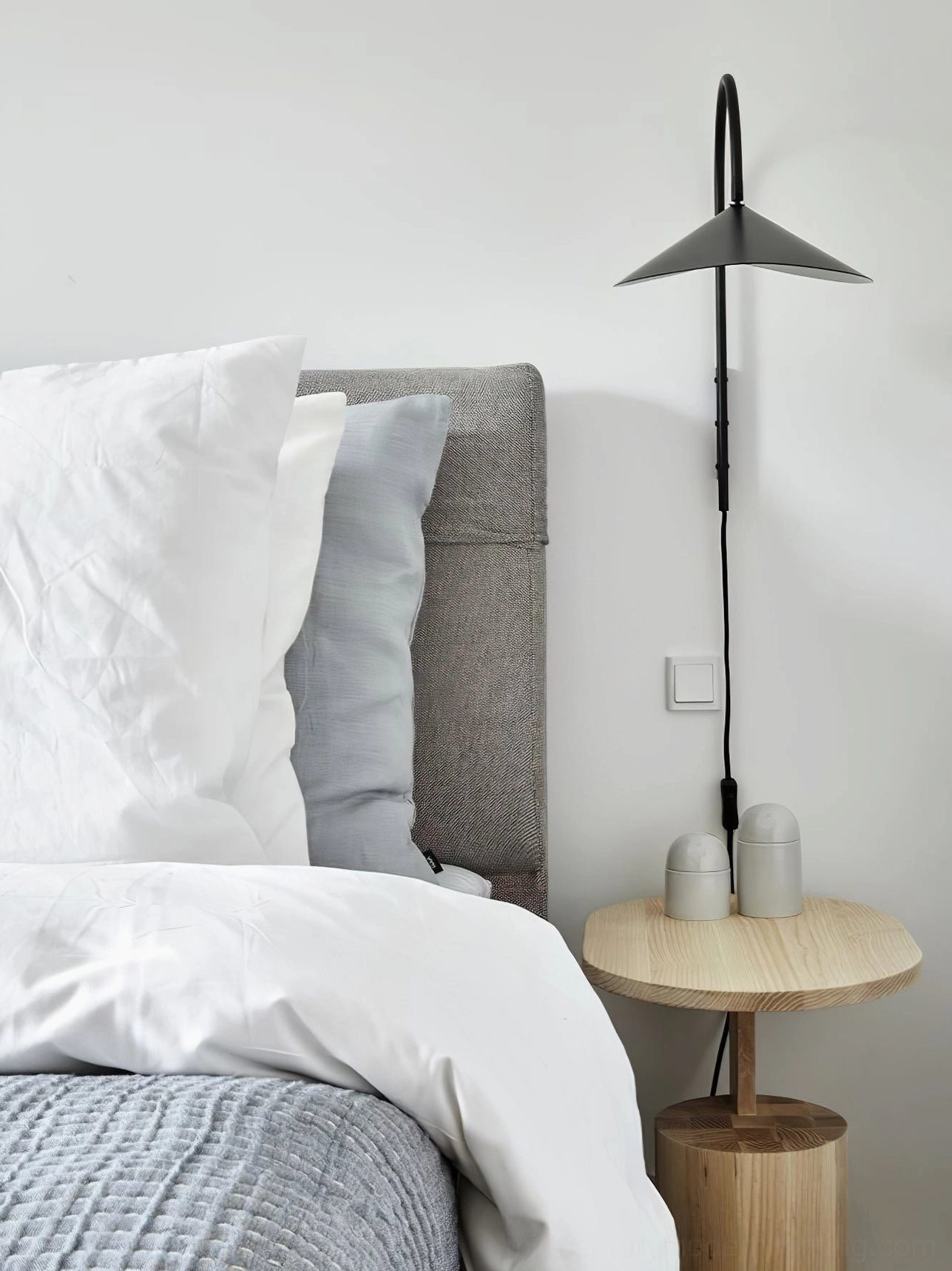 Tall black Stella wall lamp beside king bed with light wood nightstand and decorative accessories