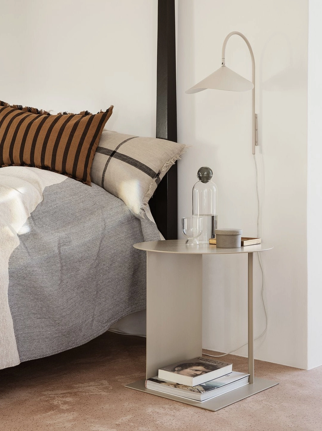 Light-toned beige Stella wall lamp beside modern bedroom bed with metal side table and decorative accents