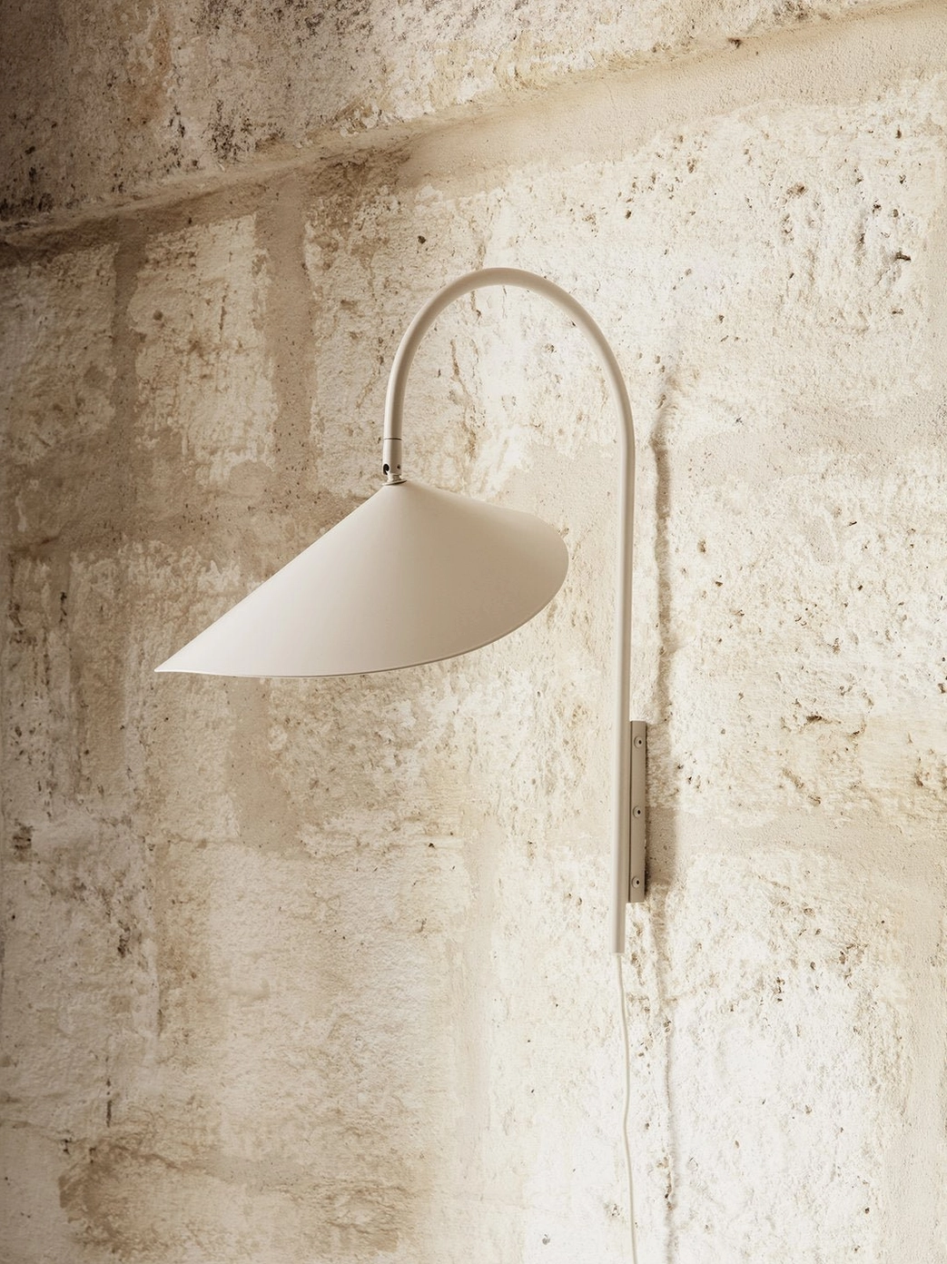 Beige neutral Stella wall lamp mounted on rough textured stone wall, minimalist matte metal design