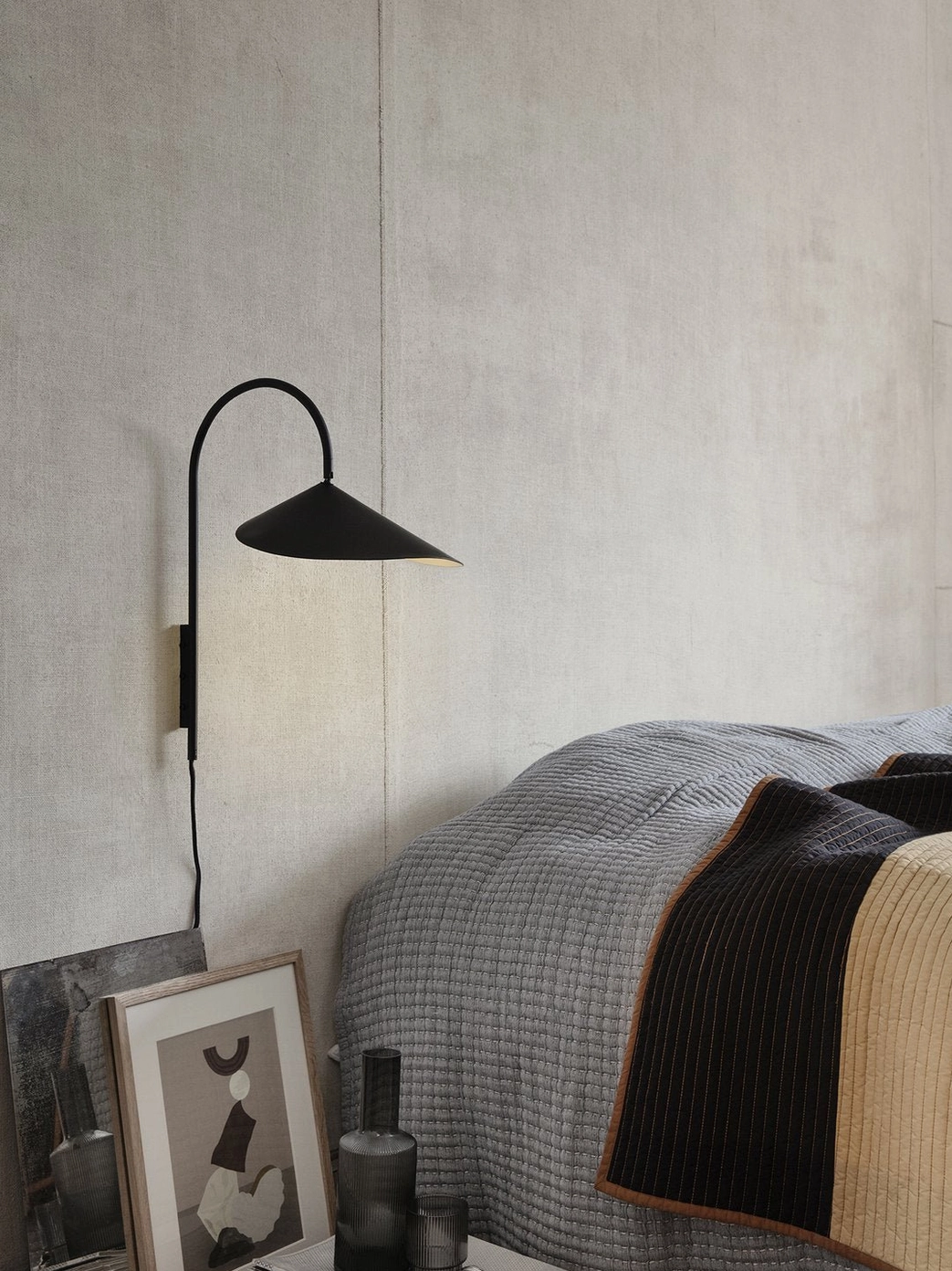 Black Stella wall lamp installed beside master bedroom bed with textured neutral bedding and minimal decor