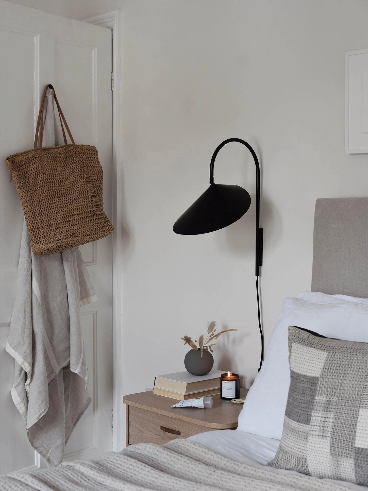 Compact Stella wall lamp in black flanking bed in small bedroom with woven tote bag styling