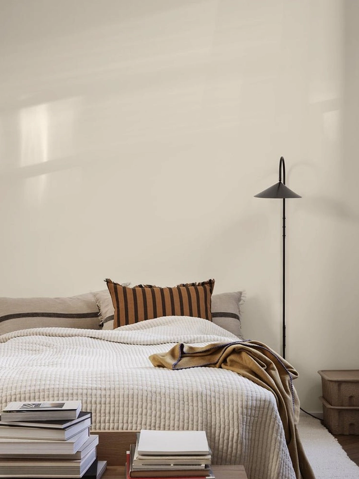 Floor-to-ceiling tall Stella 127cm wall lamp in black positioned next to stacked books in modern bedroom