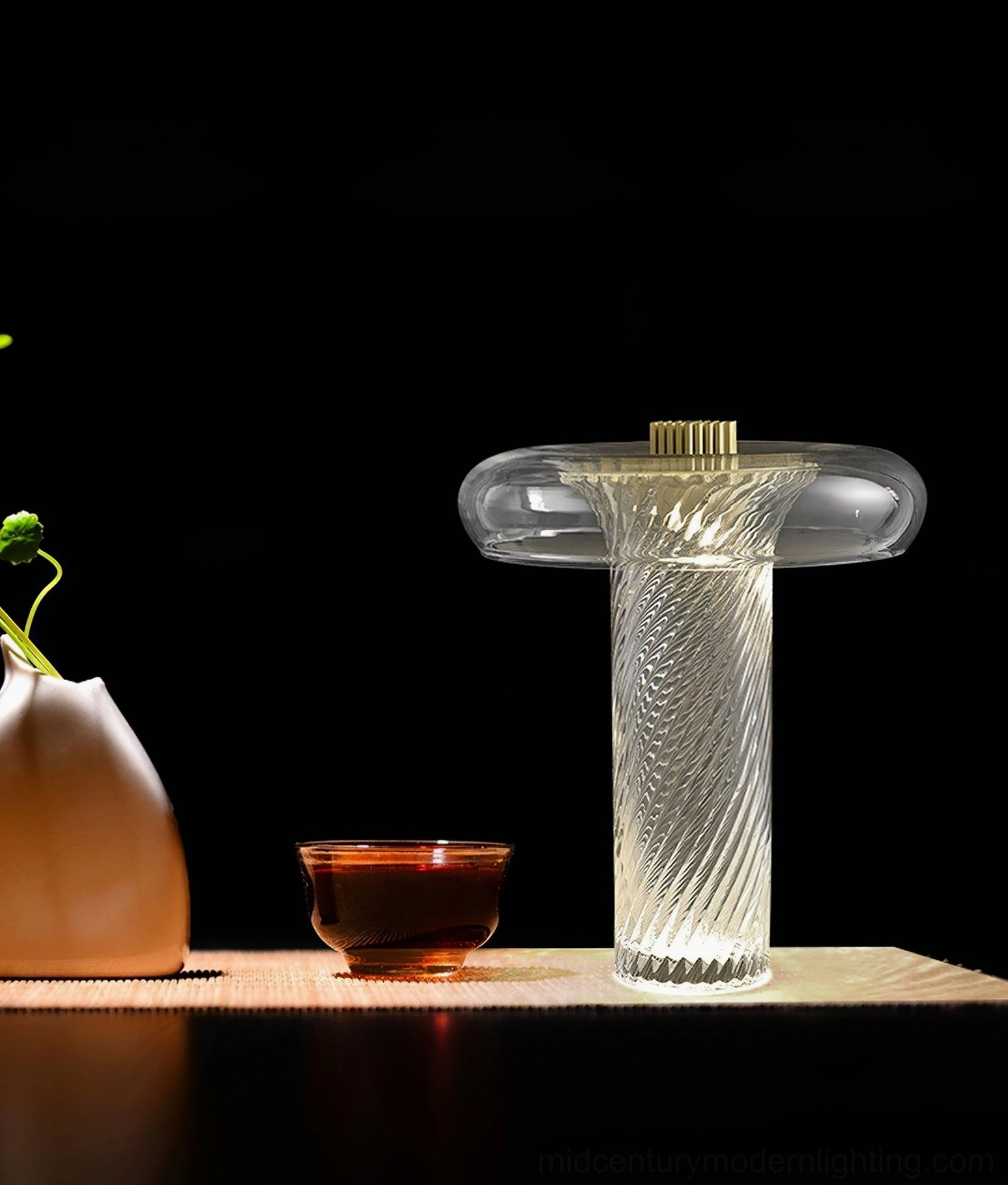 Stellar brass-topped glass table lamp paired with ceramic sculptures on dark minimalist surface