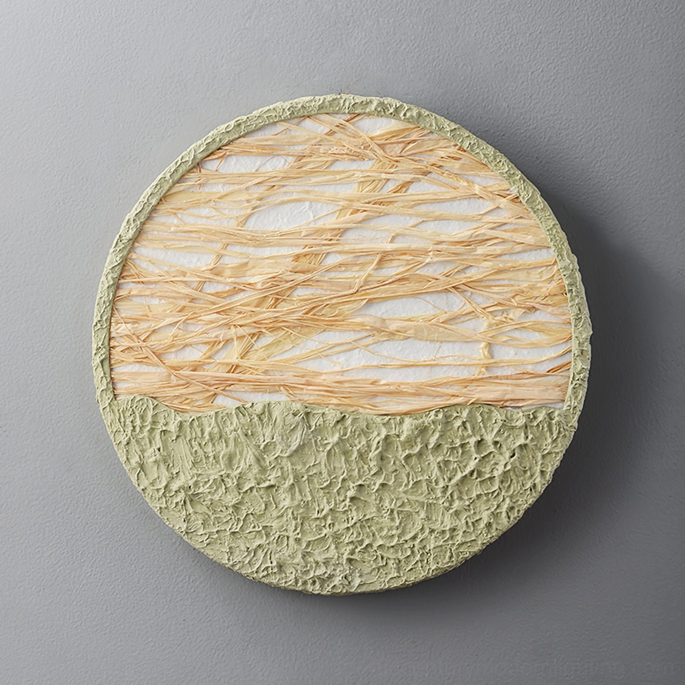 Unlit straw wall lamp on gray wall - two-tone circular design with textured light green base and natural straw weaving