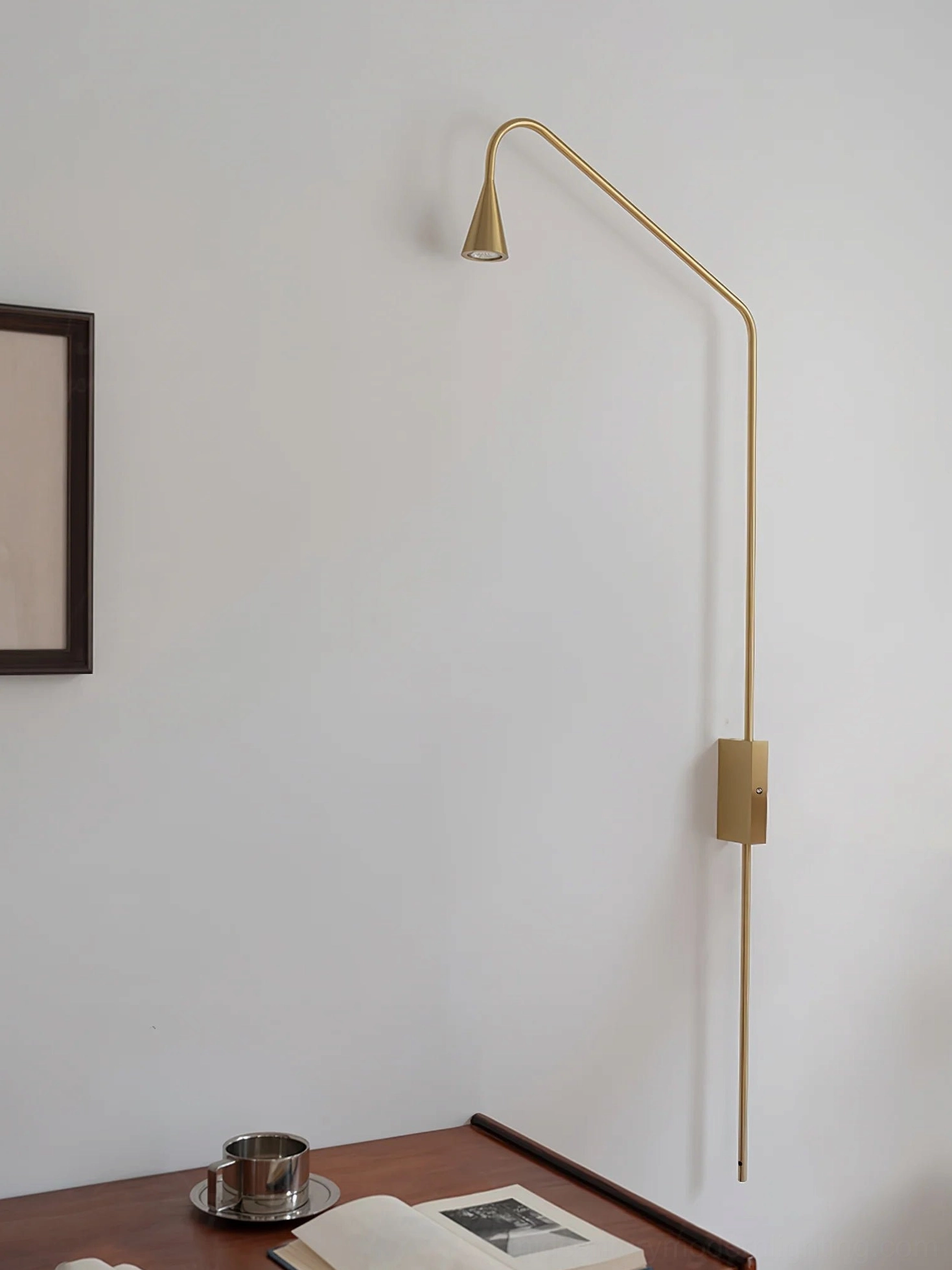 Gold brass Svarna wall lamp with adjustable curved arm, side view indoor mounted on bedroom wall with wooden furniture