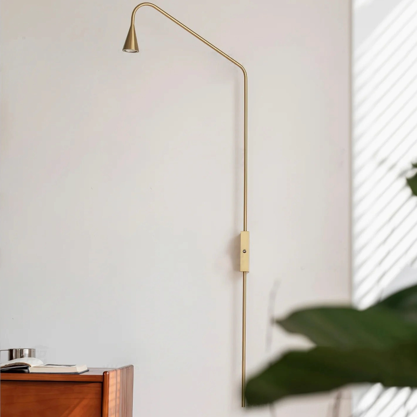 Warm gold brass Svarna wall sconce mounted indoors with natural light, Nordic minimalist bedroom reading lamp