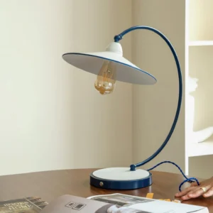 Swan Blue Table Lamp on wooden table - three-quarter side view showing sculptural curved arm and round base with blue power cord