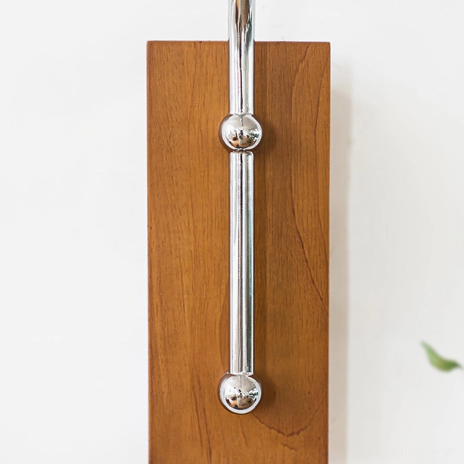 Wall mounting bracket detail of swing arm lamp featuring rectangular wooden plate with polished chrome rod and decorative spherical accents