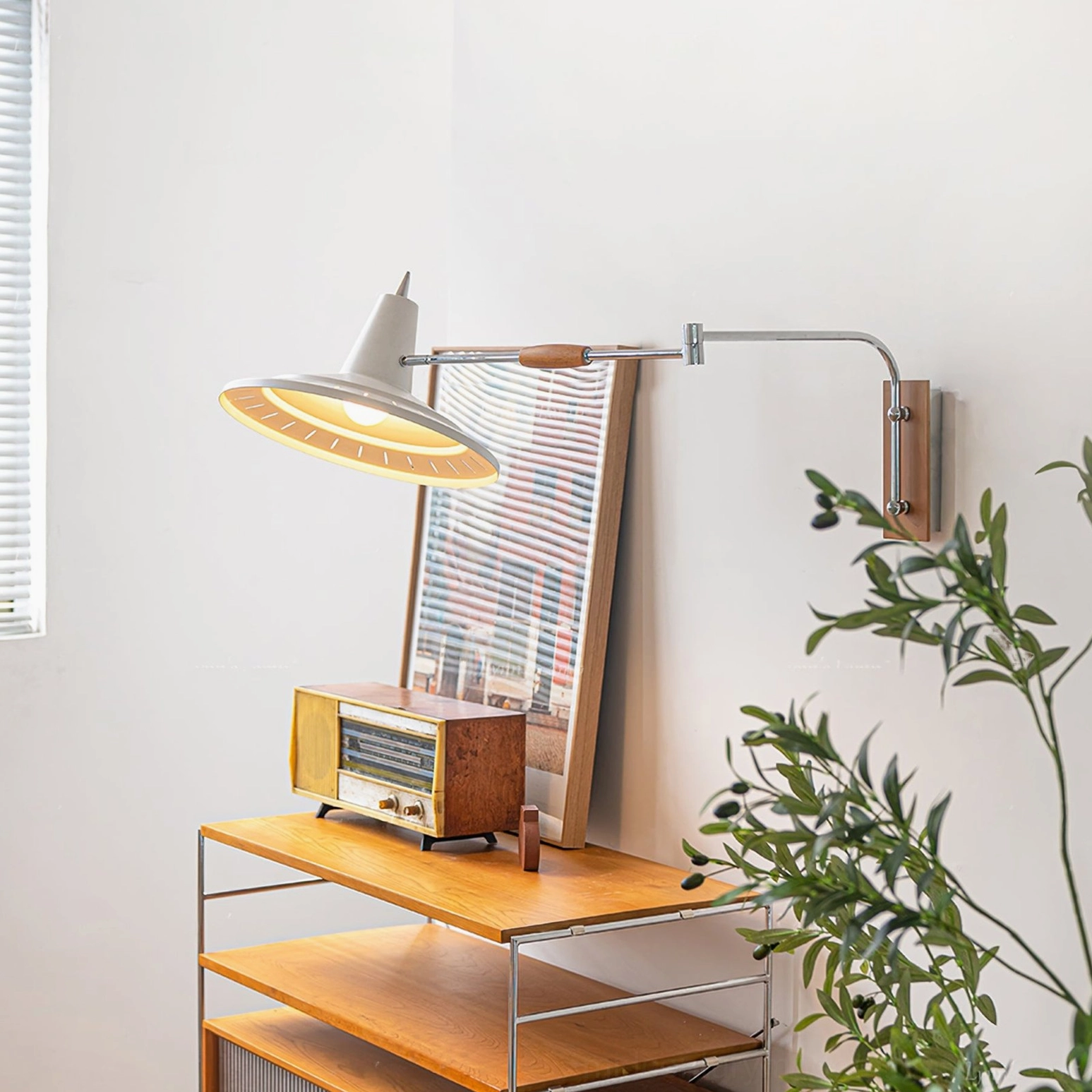 Illuminated swing arm lamp with warm yellow light in home corner featuring window blinds, green plants and mid-century modern furniture