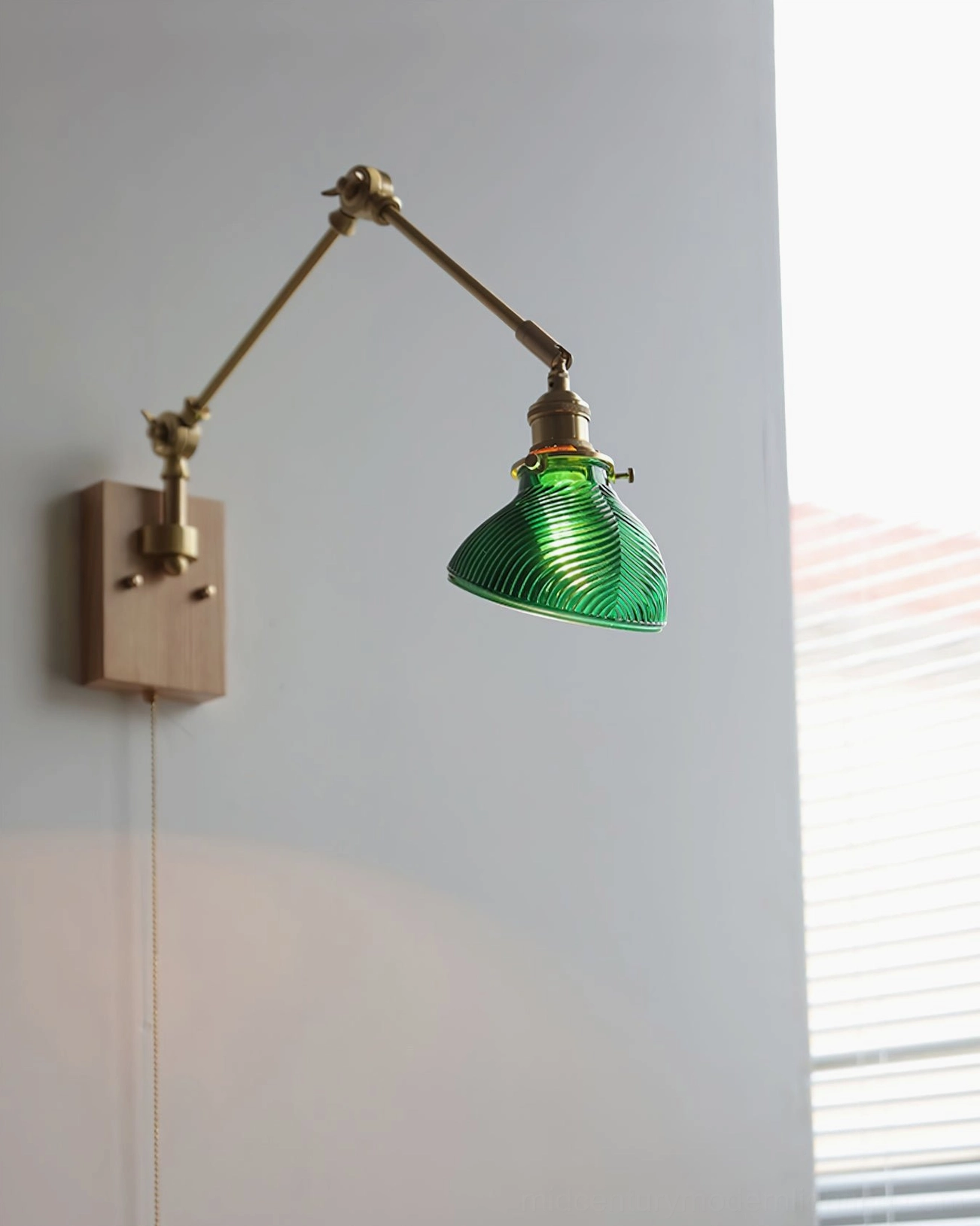 Rebell wall lamp side profile showing brass swing mechanism, light wood base, and green ribbed glass shade in home setting