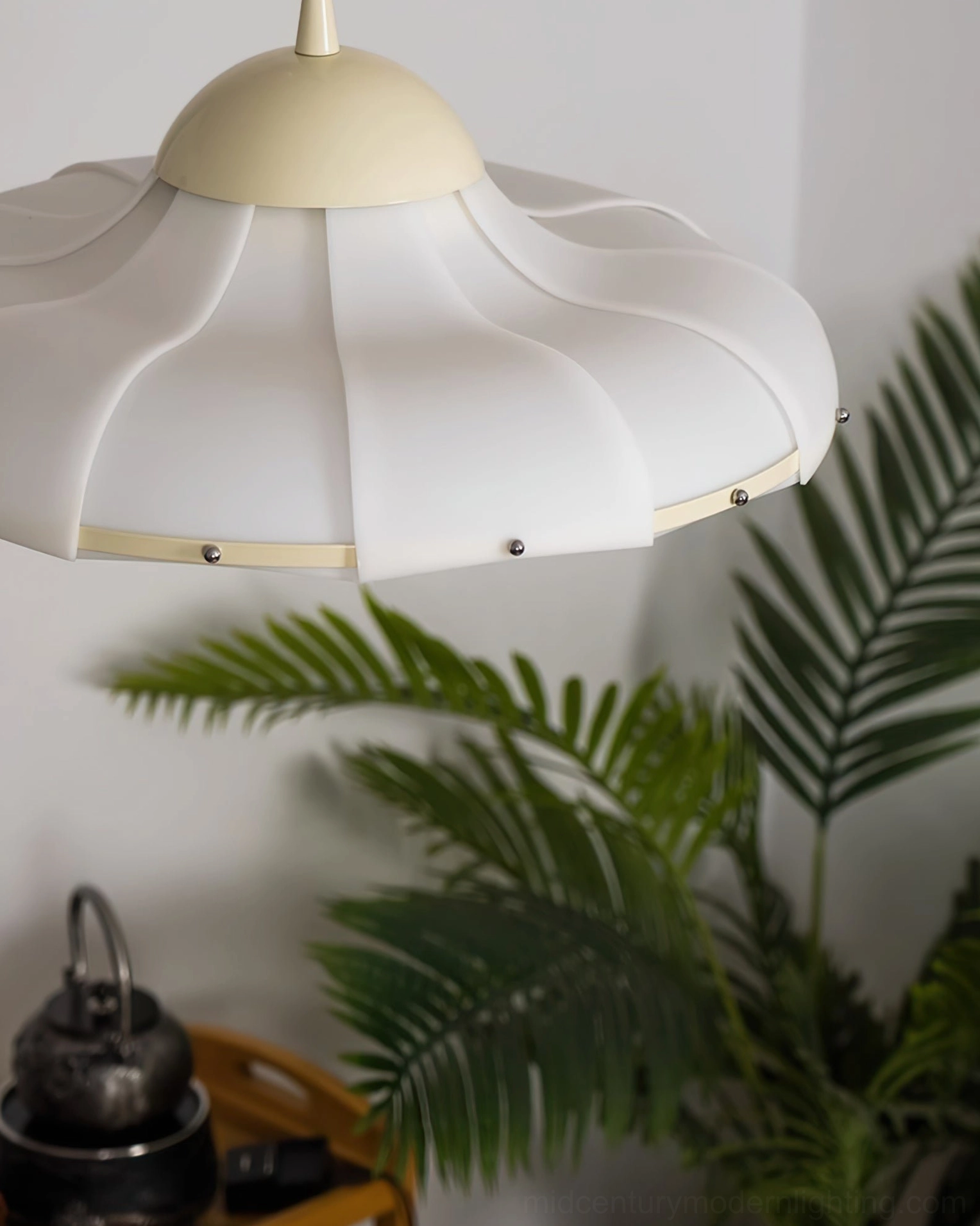 Close-up detail of swirl pendant lamp shade scalloped edge with metal fasteners and palm foliage background
