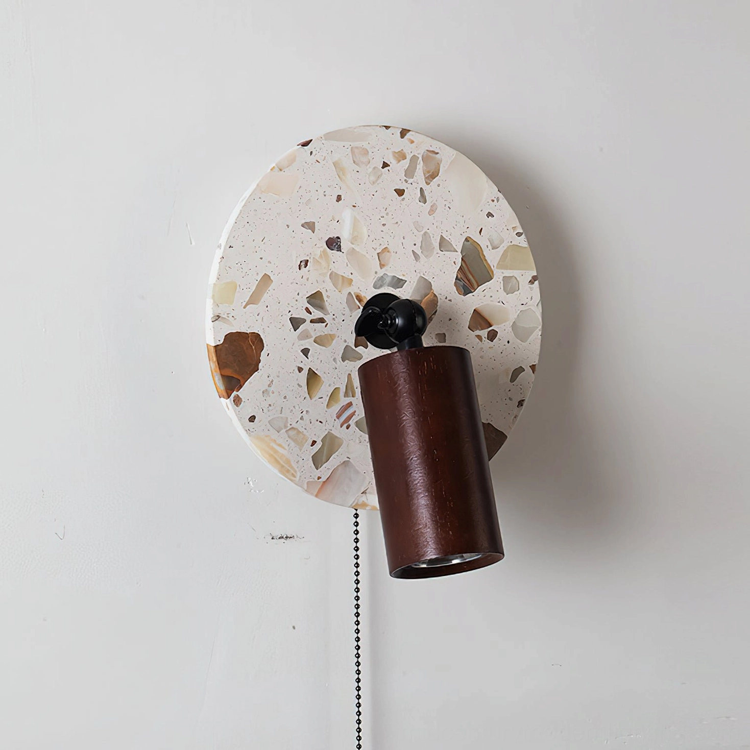 Swizzle wall lamp side view perspective showing circular terrazzo composition with warm earth tones and walnut wood support structure