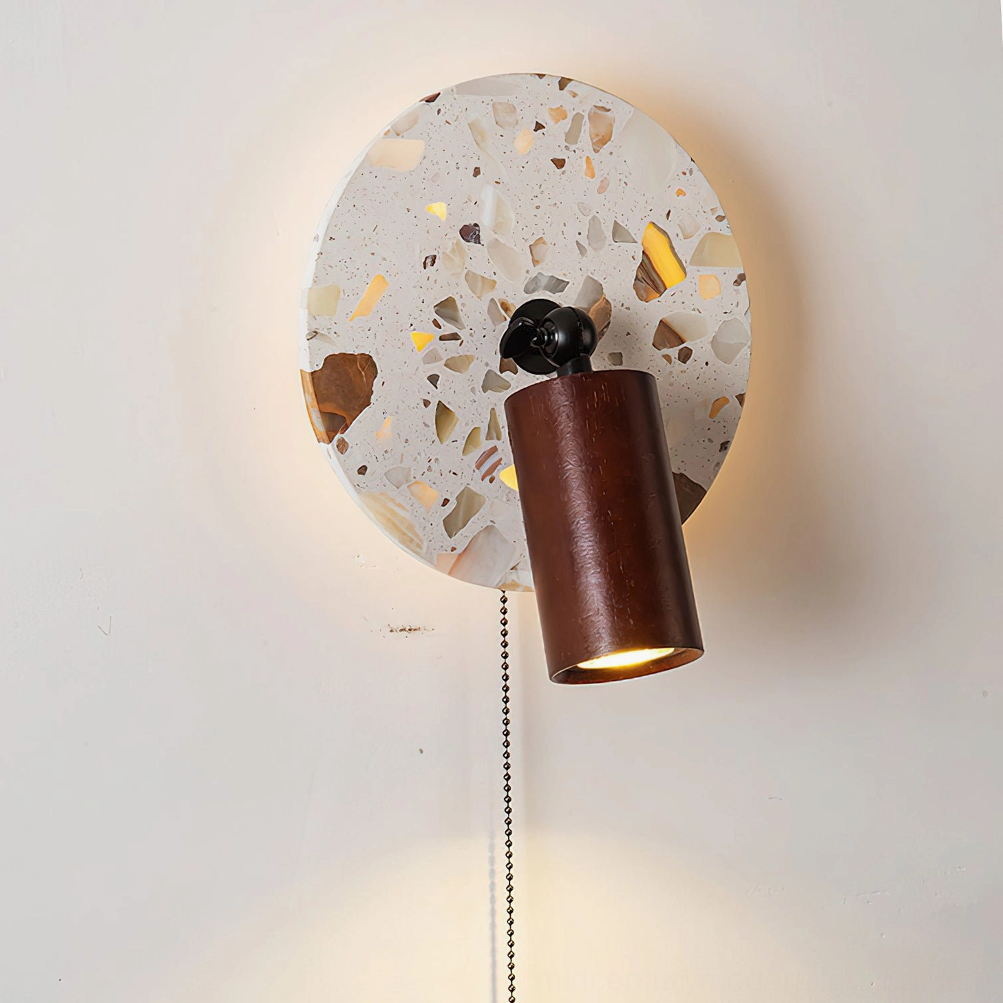 Swizzle wall lamp frontal close-up detail shot revealing terrazzo stone texture with amber fragments and black metal mounting bracket