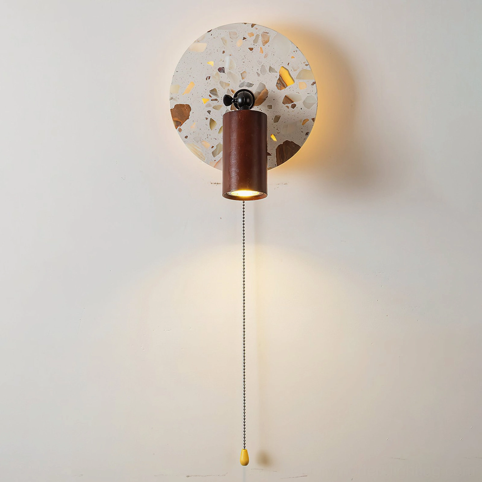 Swizzle terrazzo wall lamp direct frontal studio close-up displaying detailed stone pattern with amber mineral fragments and cylindrical lamp head
