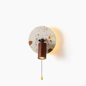 Swizzle terrazzo wall lamp front view studio shot showing circular stone backplate with amber and earth-tone mosaic pattern, walnut wood mounting bracket, and integrated LED