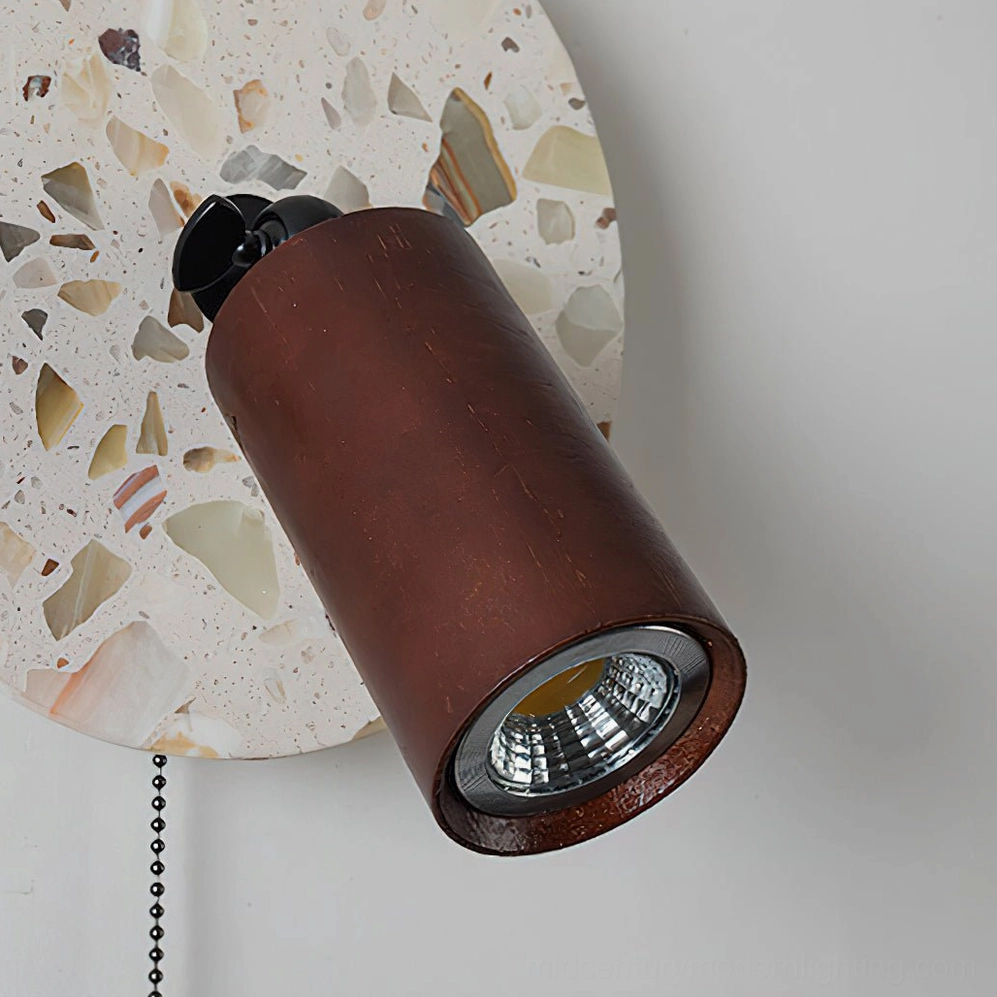 Swizzle terrazzo wall lamp three-quarter angle view revealing circular form, stone texture, and warm integrated LED illumination in studio setting