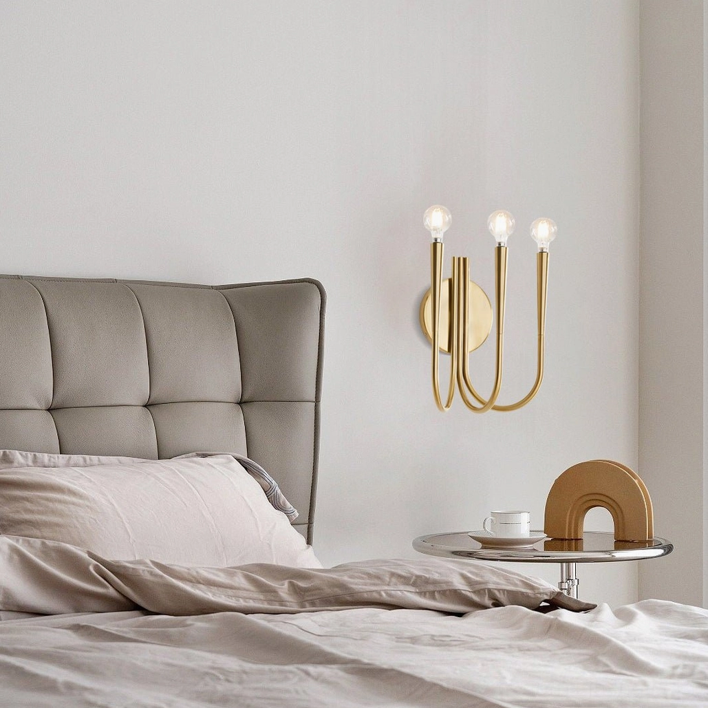 Polished brass Swoop wall sconce installed as luxury bedroom accent lighting beside tufted bed headboard