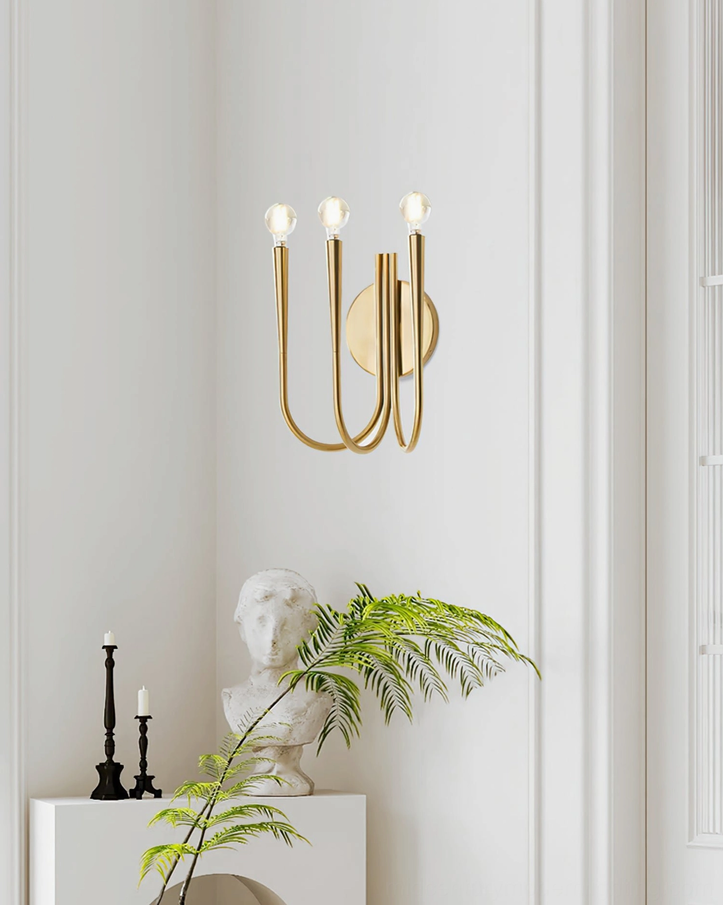 Single Swoop brass wall sconce in luxury minimalist corner setting with greenery and sculptural bust decor