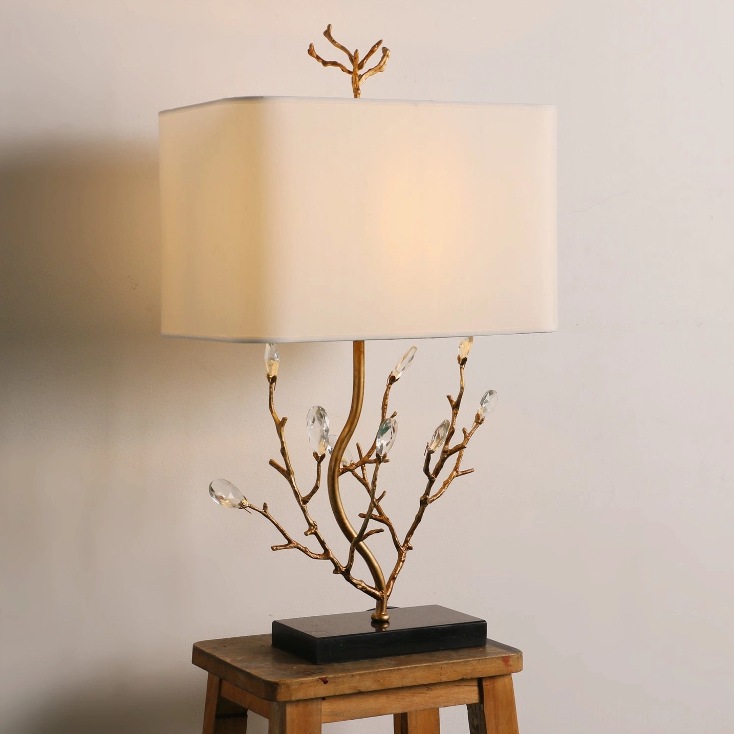 Unlit Sylvia brass branch table lamp in three-quarter view against neutral wall with wooden stool styling