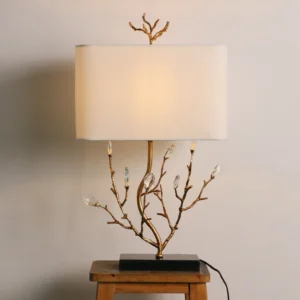 Lit Sylvia branch table lamp creating warm ambient glow, illuminated fabric shade with black square base on wooden stool