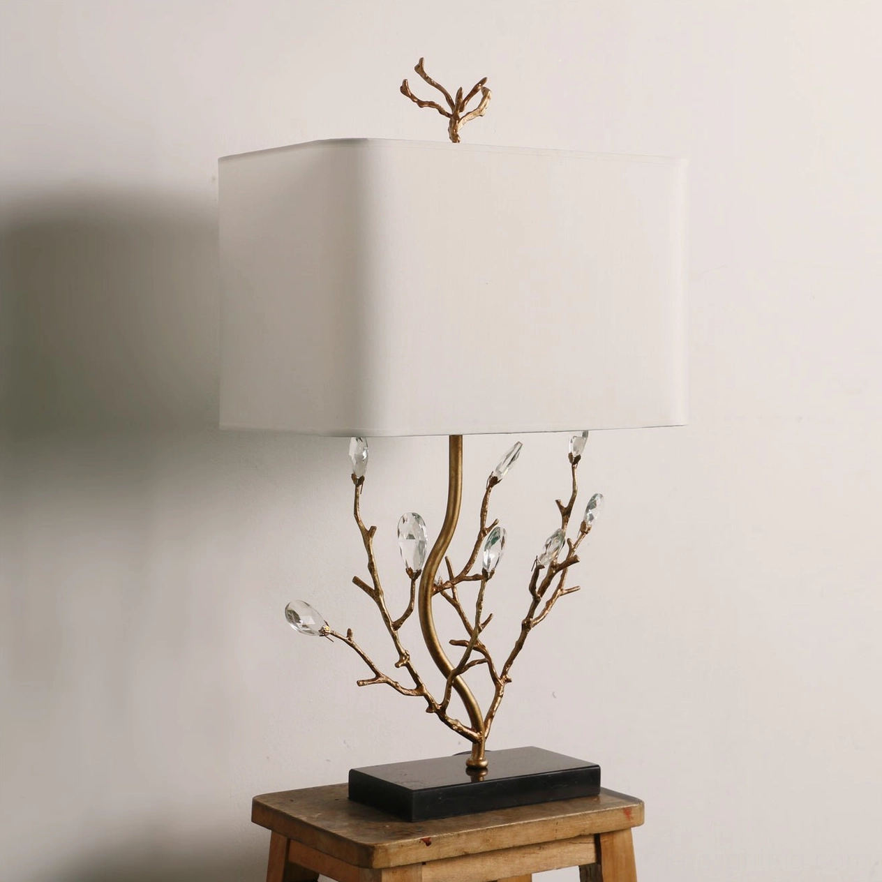 Illuminated Sylvia brass lamp frontal view with square fabric shade and black base on wooden indoor setting