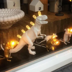 T-Rex dinosaur table lamp with warm LED lighting, displayed on retail shelf with decorative accents