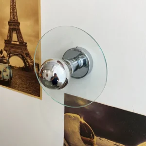 Taly chrome wall lamp side profile with illuminated glass shade against vintage poster wall