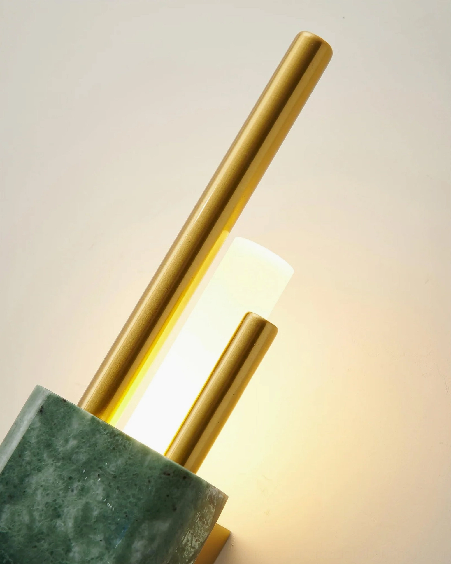 Low-angle close-up of Tanto green marble wall sconce with glowing warm white LED light and metal framework